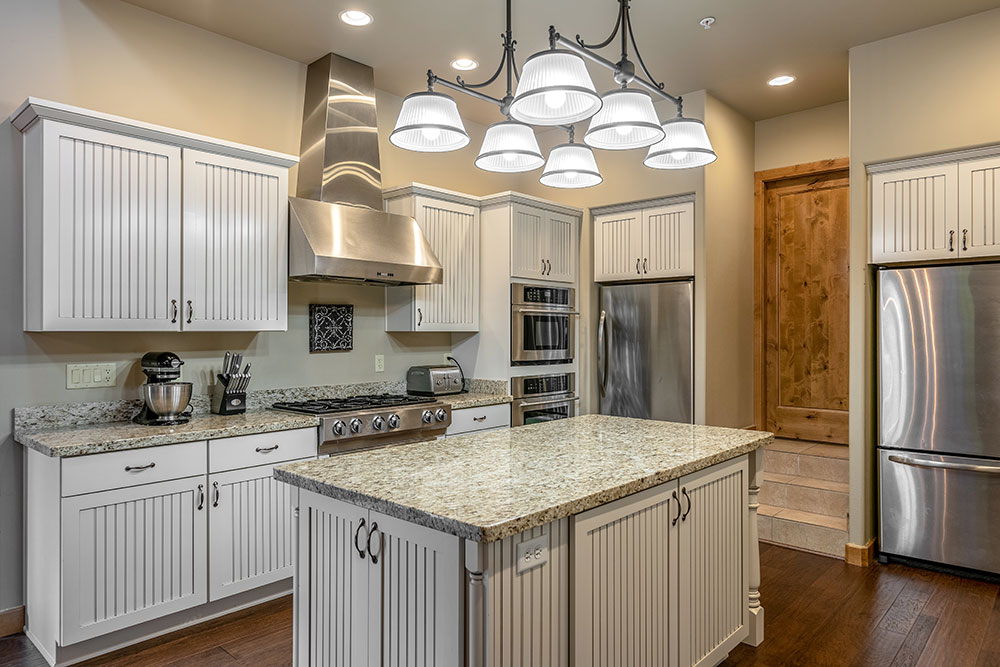 A newly remodeled Kitchen with light sage green cabinets and wood floors with granite countertops